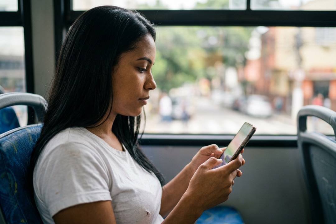 Mulher no ônibus passando o dedo na tela do celular para cortar um vídeo